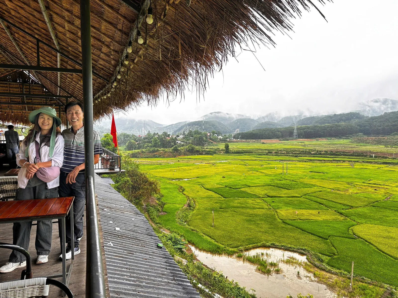 Hai du khách ở hiên nhà mái tranh nhìn ra cánh đồng lúa xanh